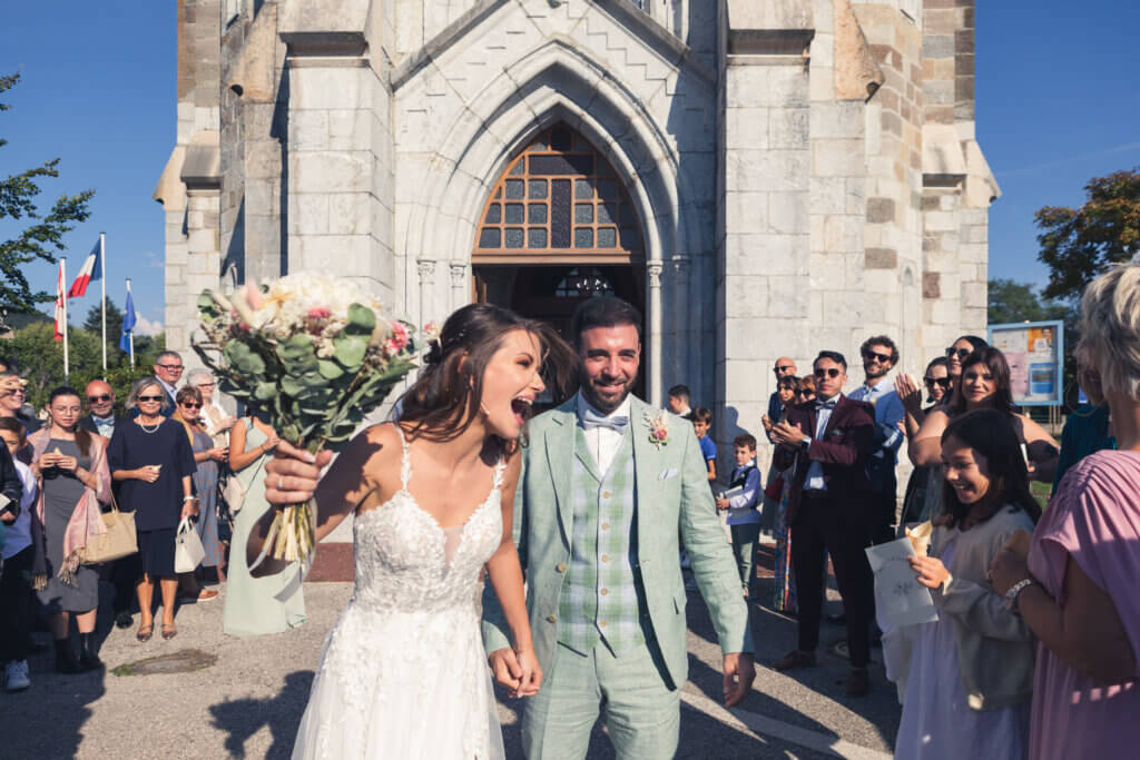 Mariés souriants sortant de l’église après la cérémonie, sous les regards de leurs invités.