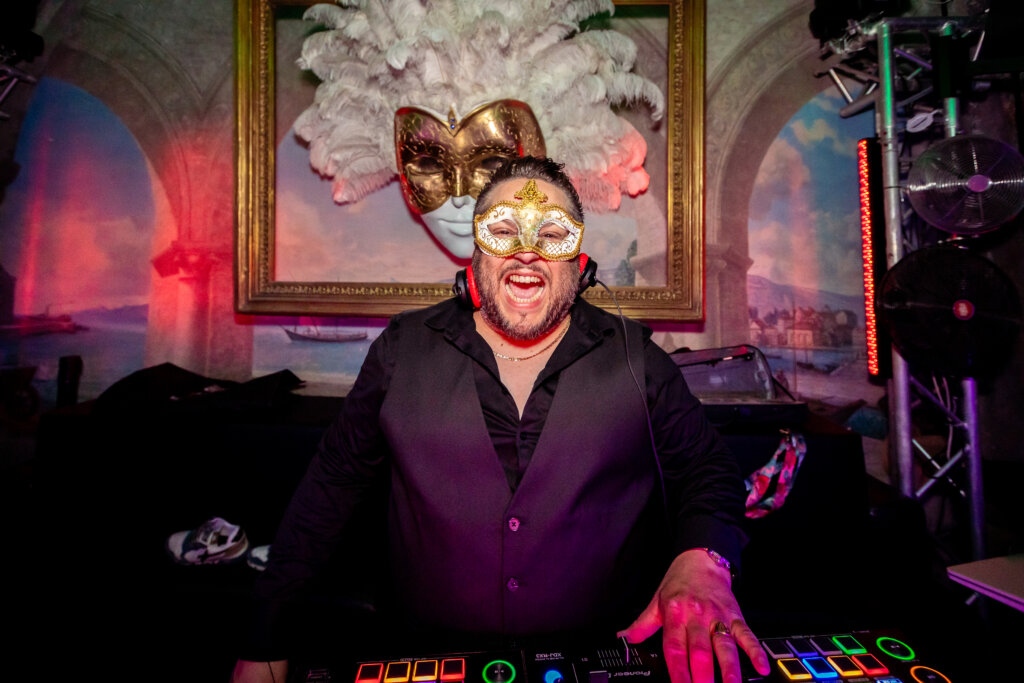 Un DJ portant un masque et un casque anime la soirée derrière sa console dans une ambiance rouge et violette.