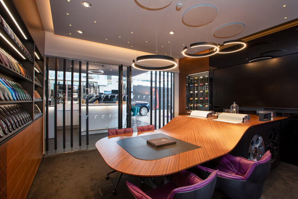 Salle de réunion haut de gamme avec grande table en bois, fauteuils colorés et éclairage design dans un showroom contemporain
