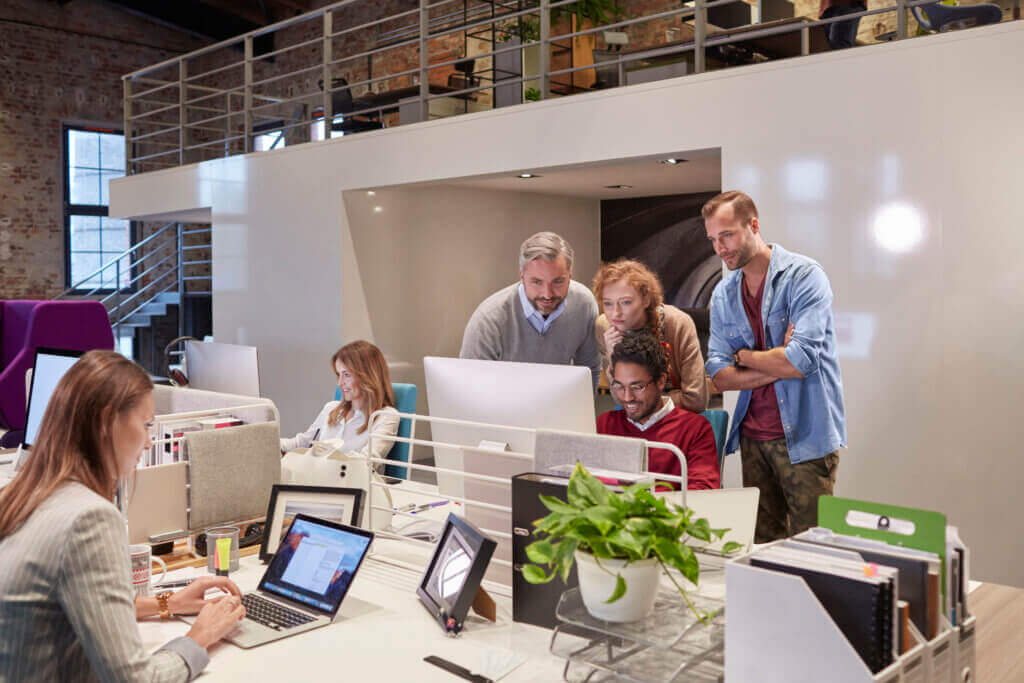 Collaborateurs réunis autour d'un écran d'ordinateur dans un open space de style loft avec mezzanine et briques apparentes