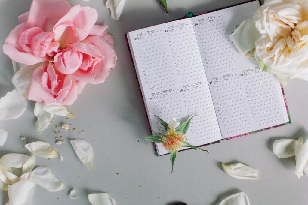 Agenda de mariage ouvert entouré de roses et pétales sur fond clair, symbolisant la préparation et le planning du jour J