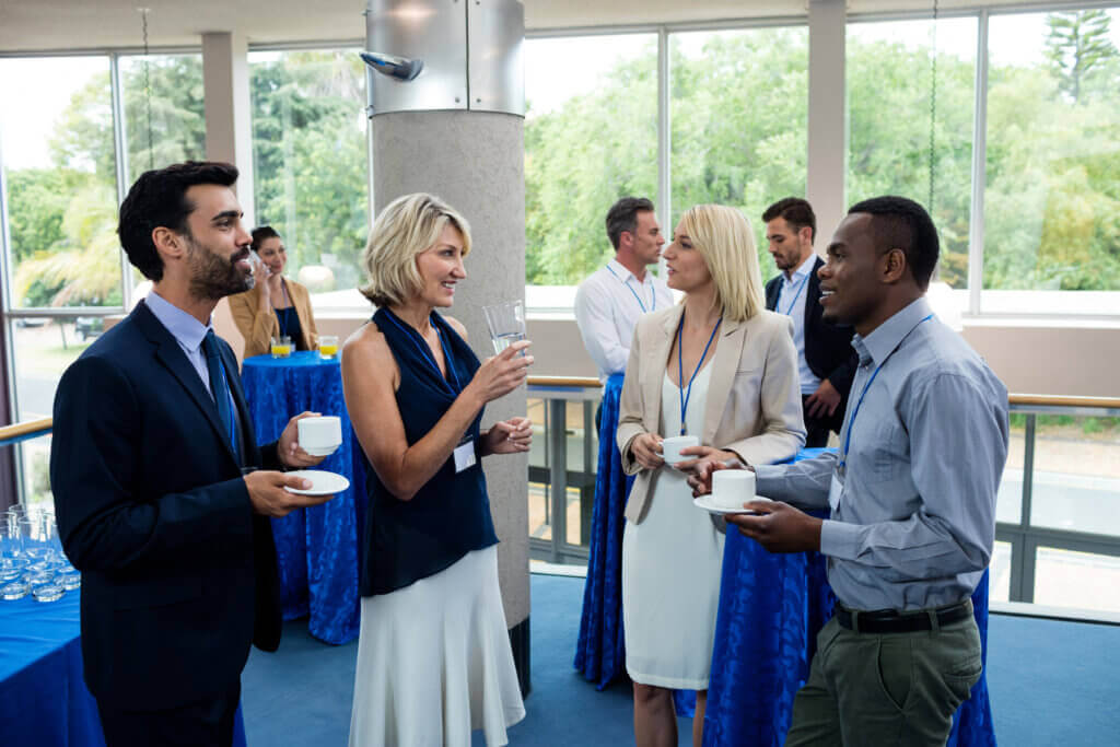 Professionnels échangeant lors d'un cocktail networking dans un espace événementiel lumineux avec grandes baies vitrées